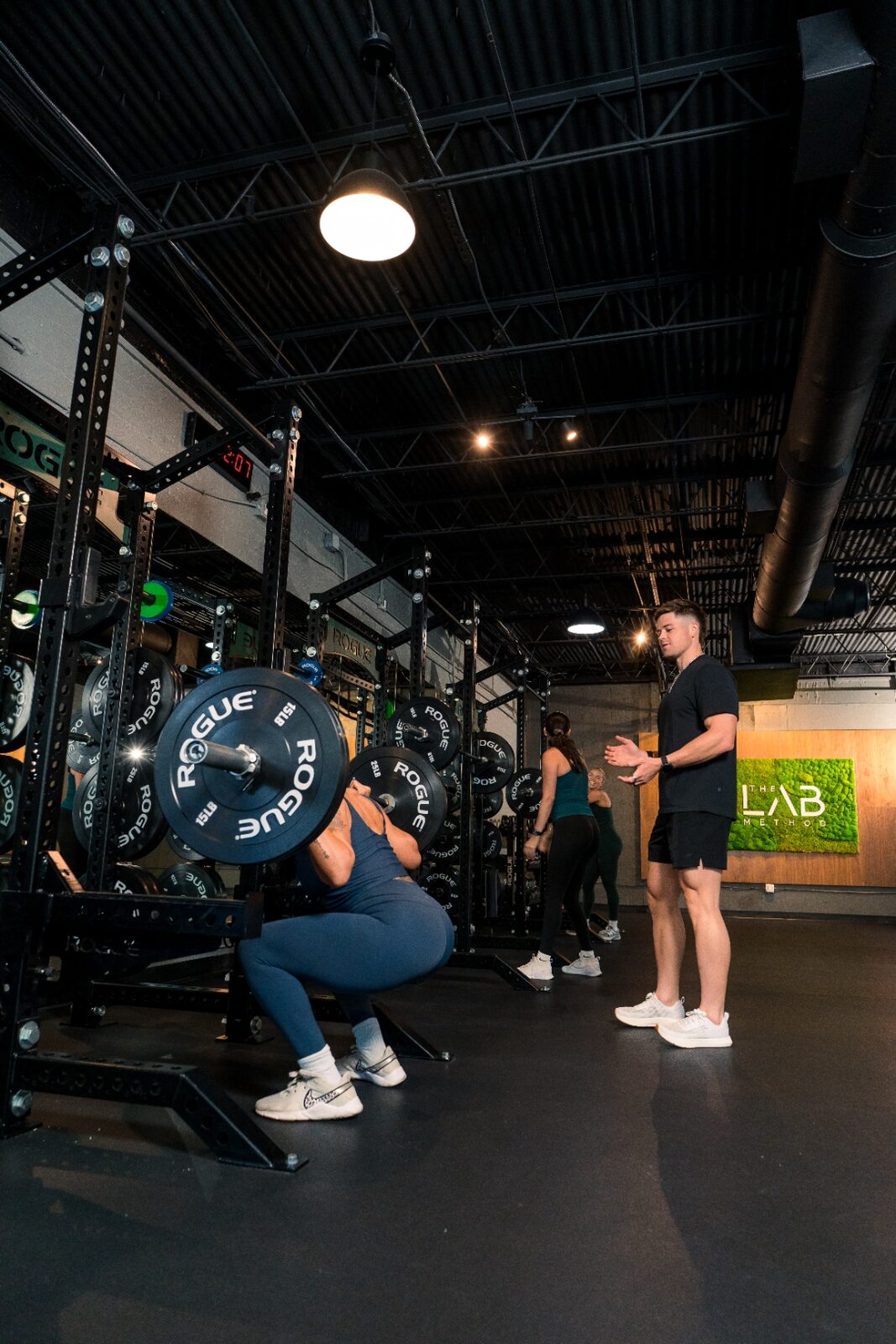 Dylan coaching a client through a barbell squat on the gym floor